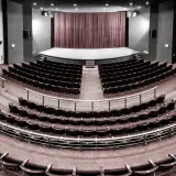 Pusta sala widowni w teatrze im. Aleksandra Sewruka w Elblągu, z rzędami czerwonych foteli i sceną w tle.