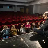 Dzieci słuchają opowieści na scenie, siedząc przed rzędem czerwonych foteli. To część repertuaru teatru Zagłębia.