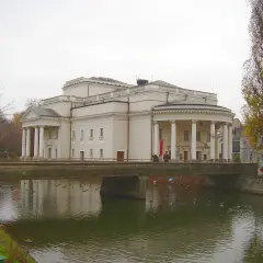 Teatr Kalisz zaprasza na spektakle. Imponujący budynek z kolumnadą nad rzeką, jesienne drzewa.
