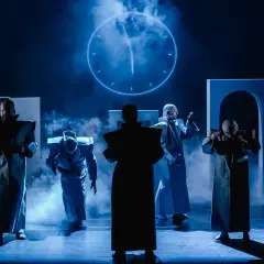 Postacie w futurystycznych strojach na scenie Teatru Arlekin w Łodzi. W tle świecący zegar.