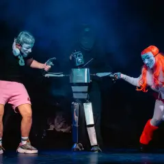 Na scenie Opolskiego Teatru Lalki i Aktora trzej artyści w maskach, jeden z nich steruje robotem.