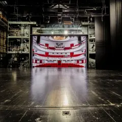 Widok na pustą widownię z czerwonymi fotelami i balkonami, widziany ze sceny. To wnętrze teatru dramatycznego w Warszawie, gotowe na spektakl.