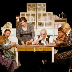 Scena z życia rodzinnego na stole obficie zastawionym jedzeniem. Sprawdź teatr Korez repertuar, by zobaczyć więcej takich przedstawień.