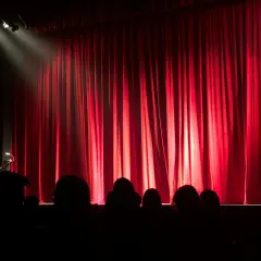 Czerwona kurtyna w teatrze współczesnym w Warszawie. Widownia w mroku, światło reflektora na scenie.