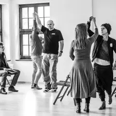 Grupa ludzi ćwiczy w sali, przygotowując się do spektaklu. To scena z życia **teatru polskiego w podziemiu**, gdzie pasja tworzy sztukę mimo trudności.