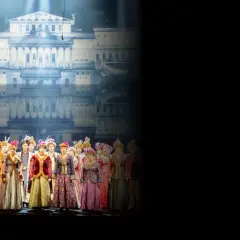 Chór w barwnych strojach historycznych na tle pałacowej scenografii. Sprawdź opera warszawa repertuar!