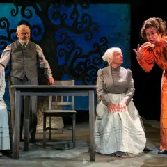 Scena z Teatru Groteska. Cztery postacie w strojach z epoki, w tym młoda dziewczyna, starszy mężczyzna i dwie kobiety, rozmawiają przy stole.