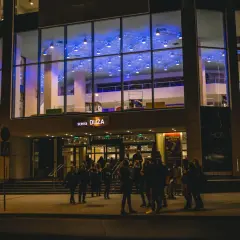 Teatr Muzyczny im. Danuty Baduszkowej nocą. Grupa ludzi czeka przed wejściem, zapowiadając nadchodzące wydarzenia.