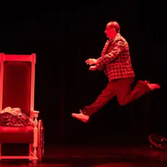 Aktor w skoku na scenie Teatru Komedia Kraków. Czerwone światło podkreśla dynamikę sceny.