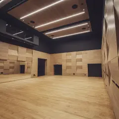 Nowoczesna sala prób w Teatrze Ludowym w Krakowie. Drewniane ściany i podłoga, lustra i oświetlenie tworzą inspirującą przestrzeń.
