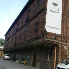 Stara ceglana kamienica z banerem "Ad Spectatores". Obok samochody i żółte krzesła.