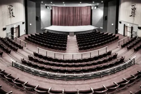 Pusta sala widowni w teatrze im. Aleksandra Sewruka w Elblągu, z rzędami czerwonych foteli i sceną w tle.