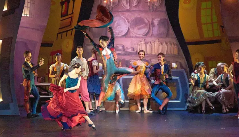 Tancerka w czerwonej sukni wiruje na scenie. W tle grupa postaci w barwnych strojach, jakby z bajki, gdzie teatr nie ma sobie równych.