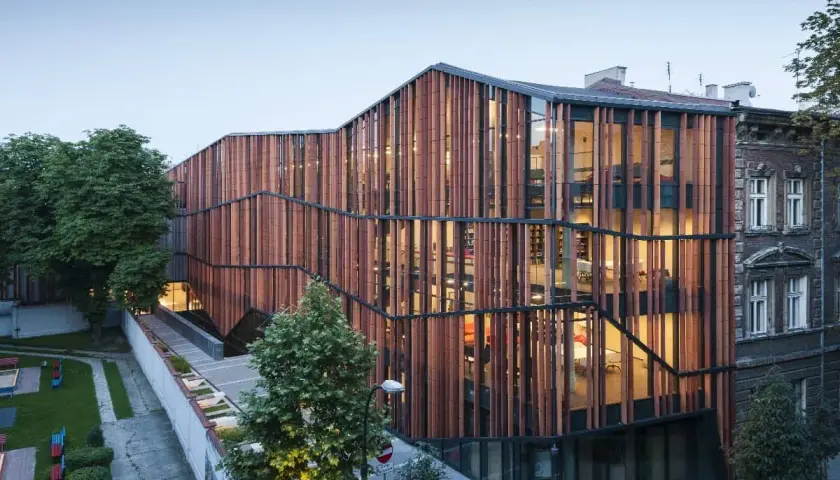 Nowoczesna architektura Małopolskiego Ogrodu Sztuki w Krakowie, z drewnianą fasadą i przeszklonymi wnętrzami, tworzy rajską oazę dla kultury.