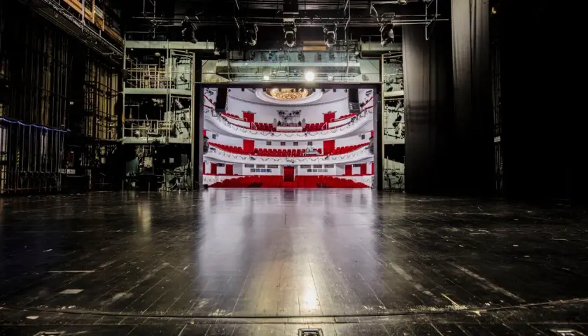 Widok na pustą widownię z czerwonymi fotelami i balkonami, widziany ze sceny. To wnętrze teatru dramatycznego w Warszawie, gotowe na spektakl.