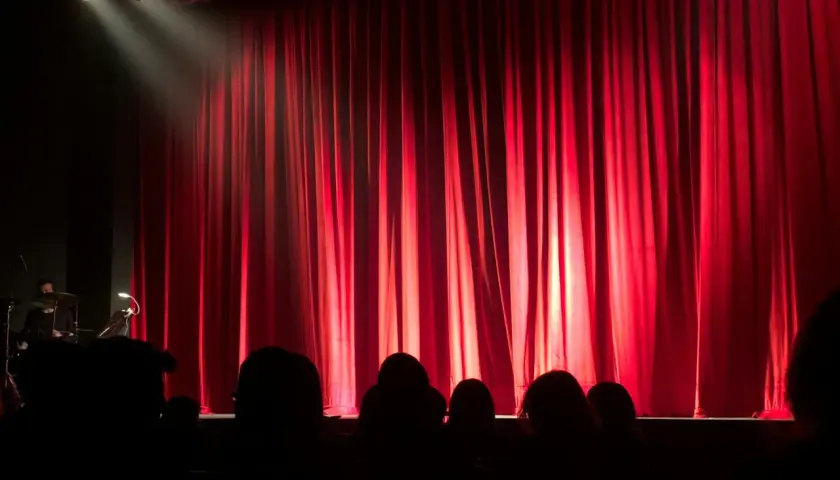 Czerwona kurtyna w teatrze współczesnym w Warszawie. Widownia w mroku, światło reflektora na scenie.