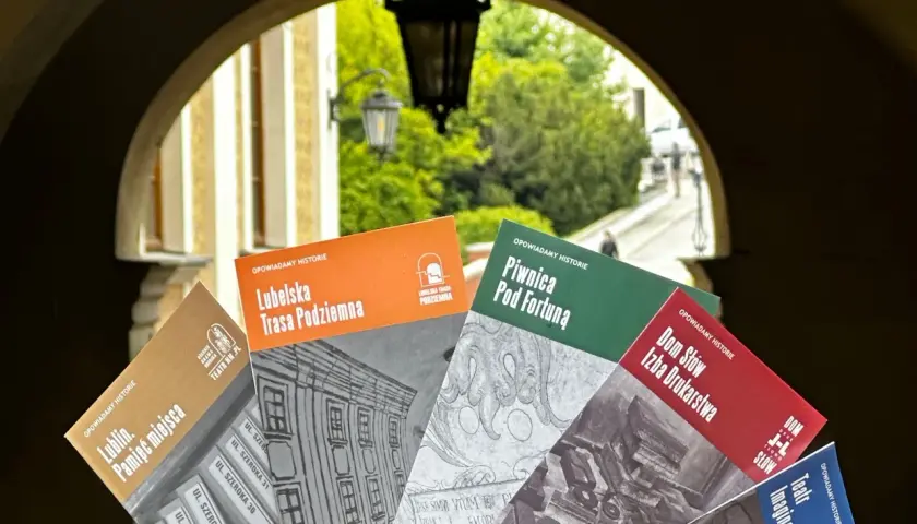 Książki o historii Lublina, m.in. "Lubelska Trasa Podziemna" i "Piwnica Pod Fortuną", prezentowane na tle bramy. Teatr NN Lublin zaprasza do odkrywania przeszłości.
