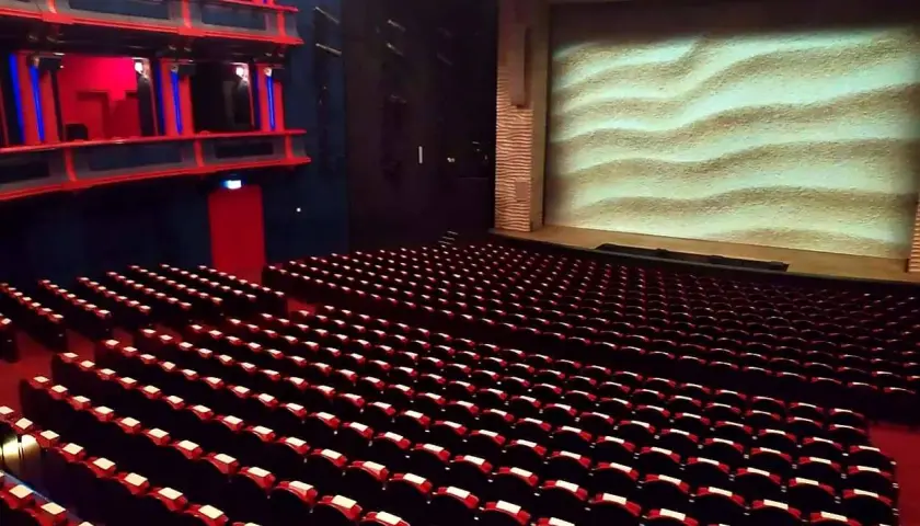 Puste rzędy czerwonych foteli w teatrze, z widownią i sceną z piaskowym tłem. Gdzie jest teatr Roma?