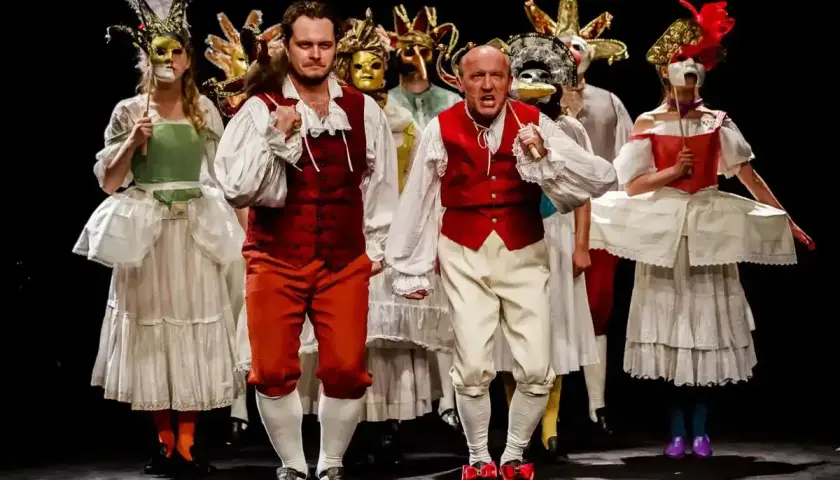 Aktorzy w barwnych strojach i maskach na scenie Teatru im. Jaracza w Warszawie.