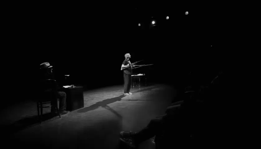 Na scenie Teatru Rondo w Słupsku kobieta z karabinami, mężczyzna w kapeluszu siedzi przy biurku.