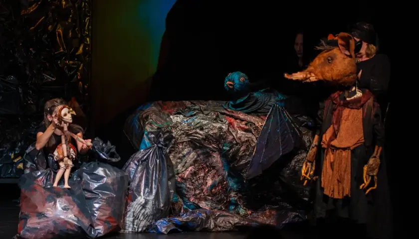 Na scenie teatru lalki i aktora w Łomży, dziewczynka animuje drewnianą lalkę, obok niej ptak i postać z głową zwierzęcia.