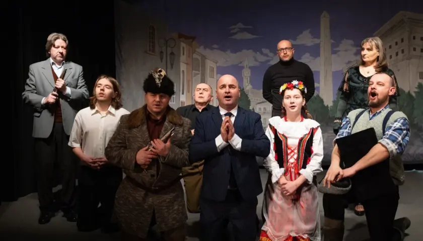 Aktorzy na scenie, w strojach z epoki, tworzą teatr ciut frapujący. W tle malowana miejska panorama.