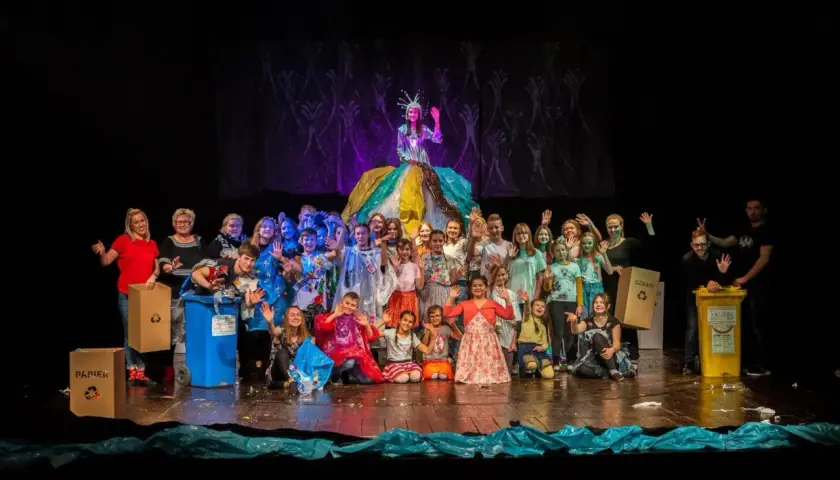 Uczestnicy studia teatralnego Gorzów pozują na scenie z kolorowymi strojami i koszami do segregacji śmieci.