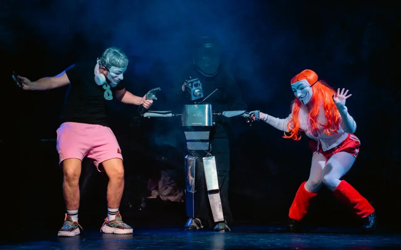 Na scenie Opolskiego Teatru Lalki i Aktora trzej artyści w maskach, jeden z nich steruje robotem.