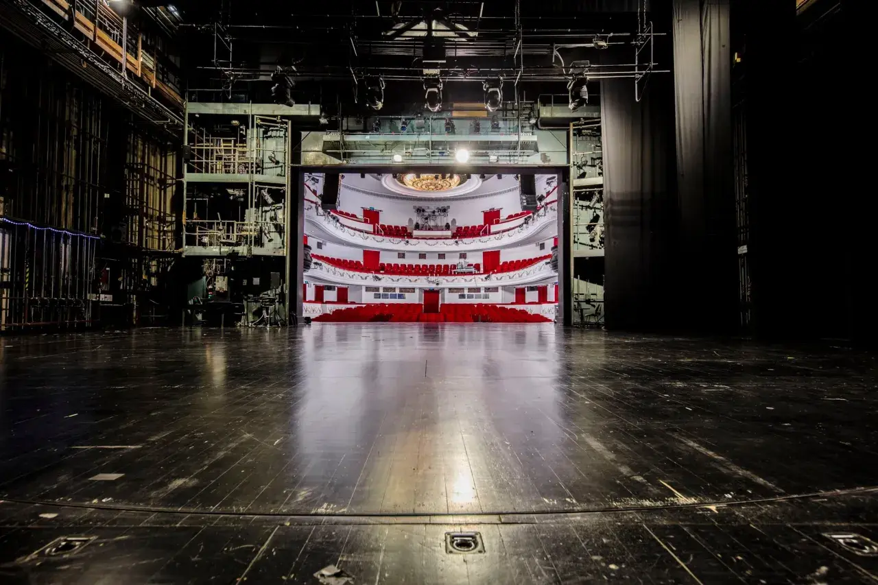 Widok na pustą widownię z czerwonymi fotelami i balkonami, widziany ze sceny. To wnętrze teatru dramatycznego w Warszawie, gotowe na spektakl.