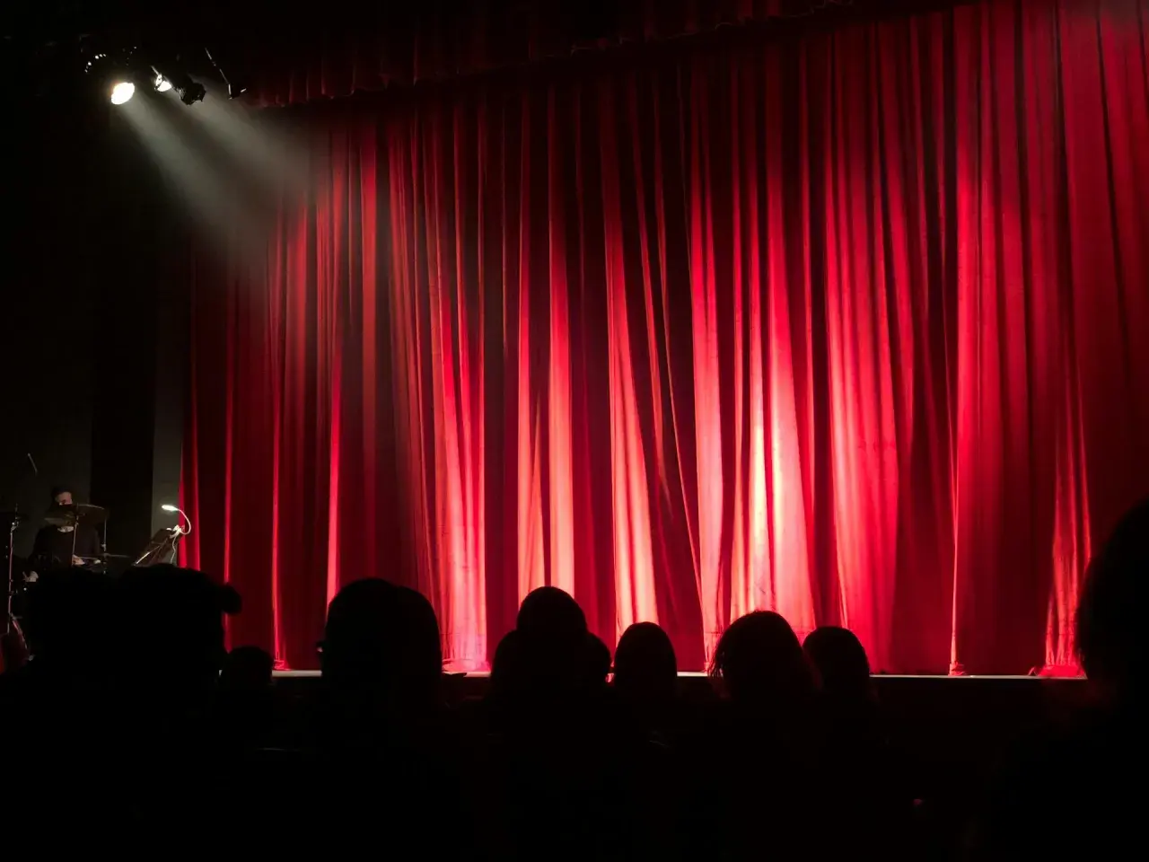 Czerwona kurtyna w teatrze współczesnym w Warszawie. Widownia w mroku, światło reflektora na scenie.