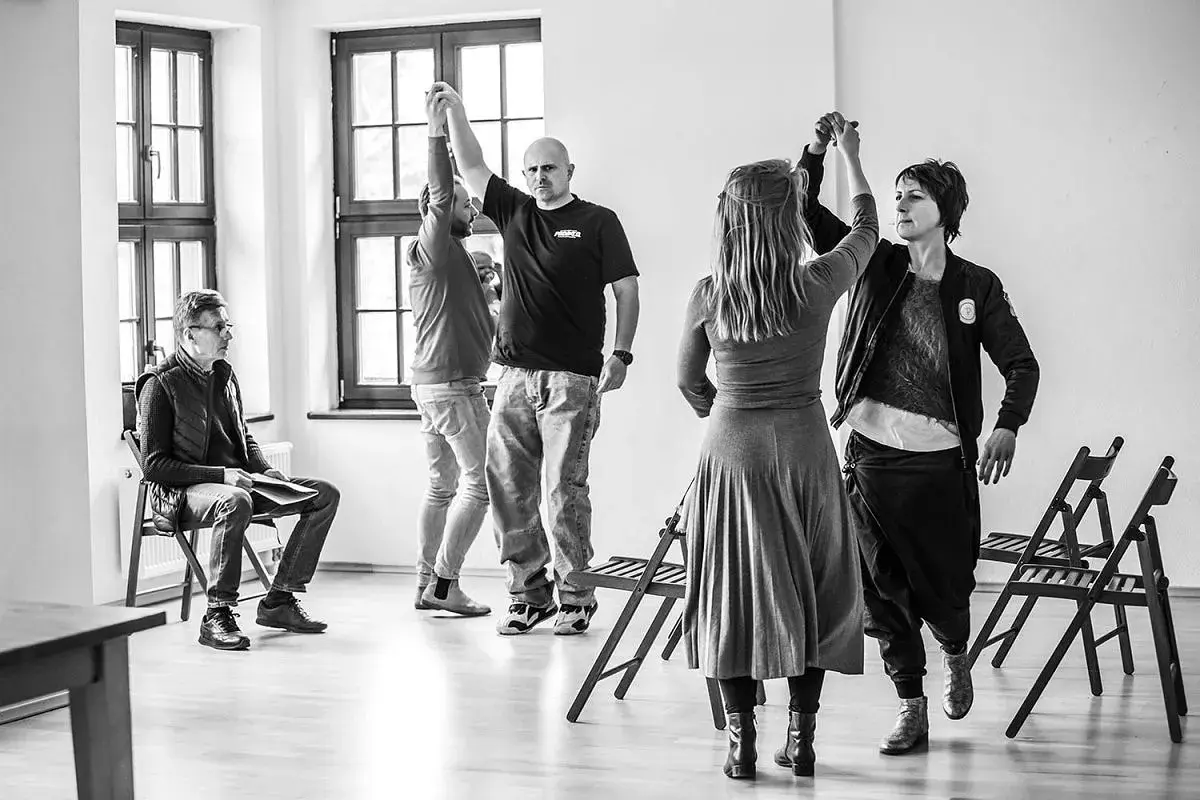 Grupa ludzi ćwiczy w sali, przygotowując się do spektaklu. To scena z życia **teatru polskiego w podziemiu**, gdzie pasja tworzy sztukę mimo trudności.