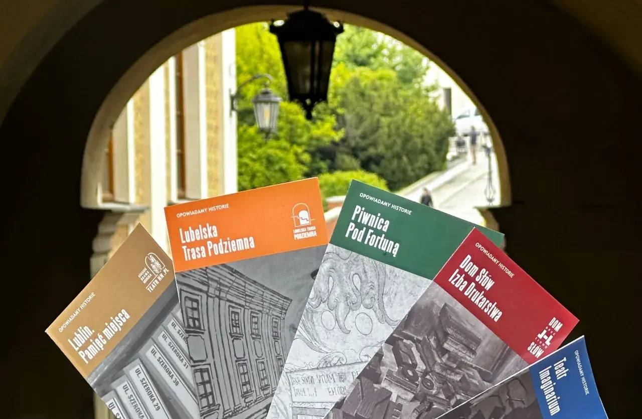 Książki o historii Lublina, m.in. "Lubelska Trasa Podziemna" i "Piwnica Pod Fortuną", prezentowane na tle bramy. Teatr NN Lublin zaprasza do odkrywania przeszłości.