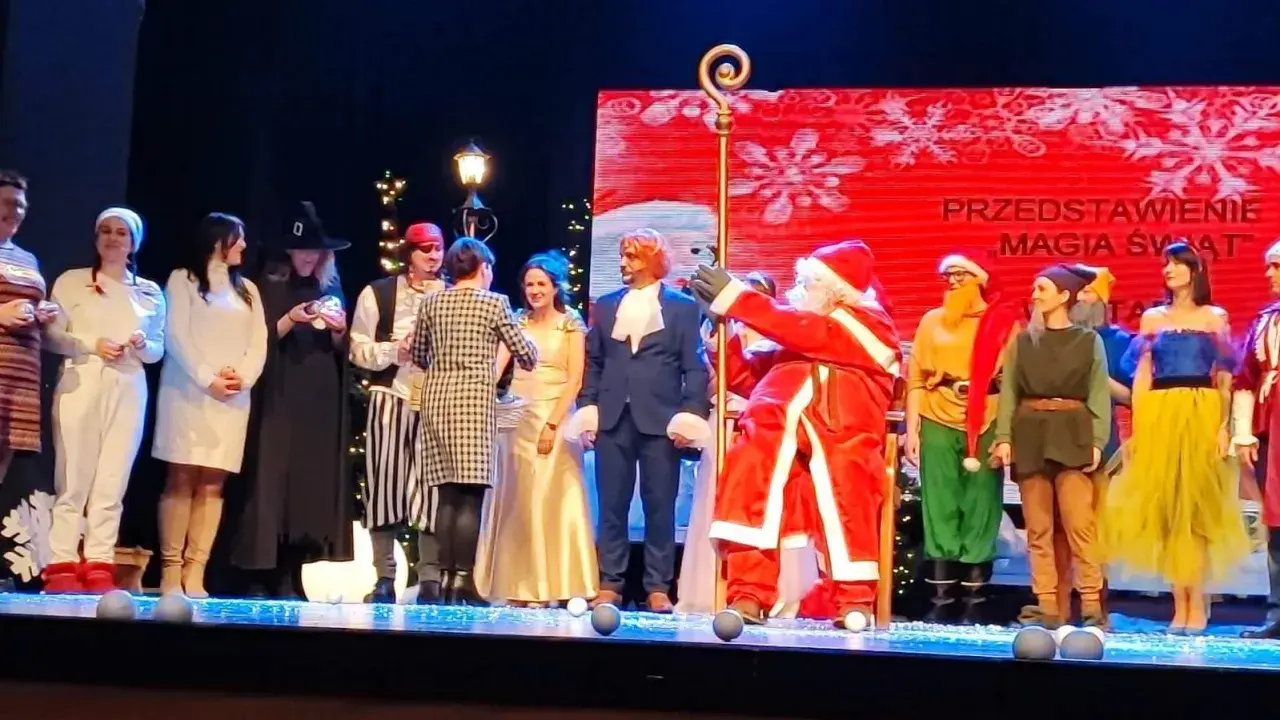Aktorzy w strojach świątecznych i bajkowych na scenie, w tym Święty Mikołaj.
