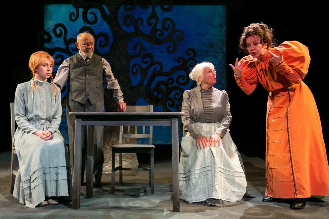 Scena z Teatru Groteska. Cztery postacie w strojach z epoki, w tym młoda dziewczyna, starszy mężczyzna i dwie kobiety, rozmawiają przy stole.