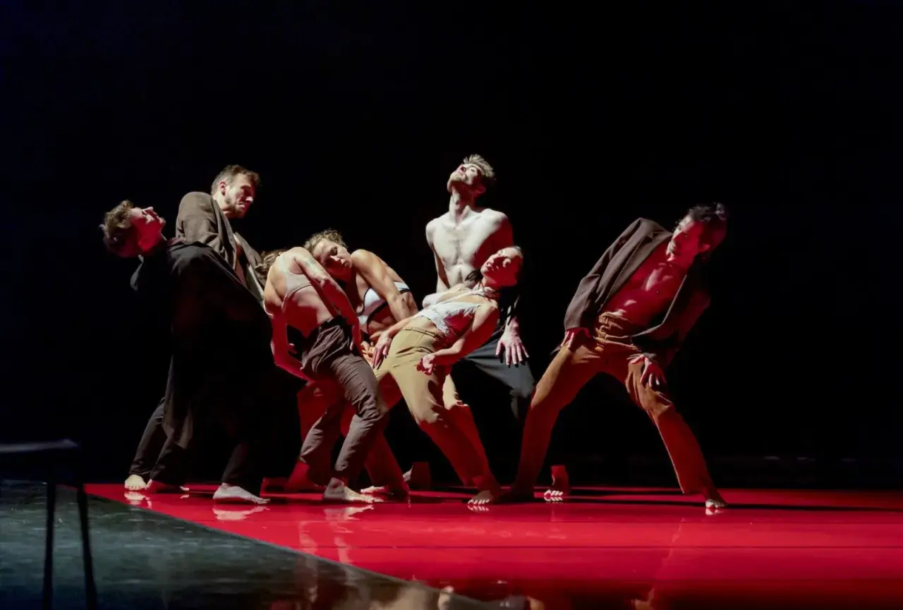 Tancerze Teatru Tańca Rozbark w dynamicznej choreografii na czerwonej scenie.