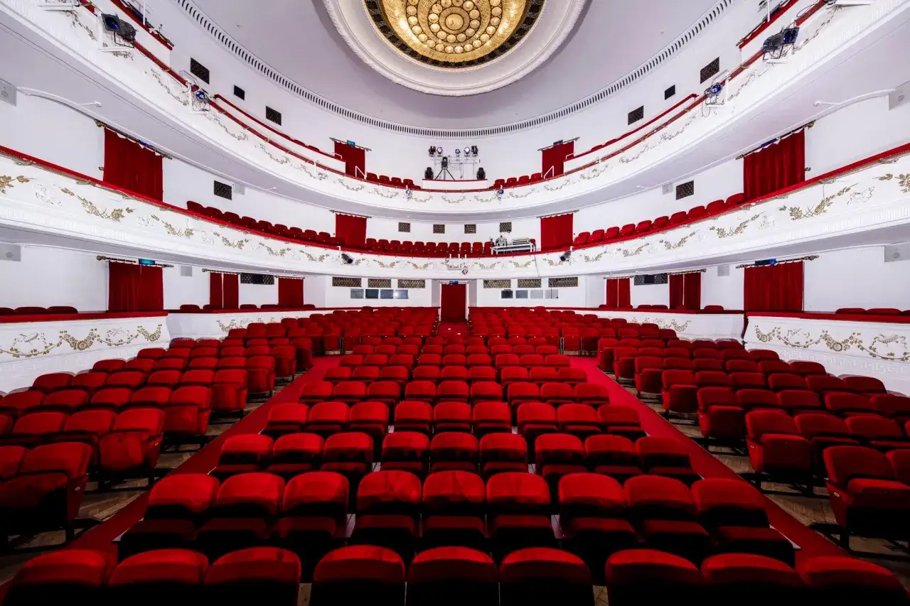Widok na wnętrze teatru dramatycznego w Warszawie. Czerwone fotele i aksamitne zasłony tworzą elegancką atmosferę.