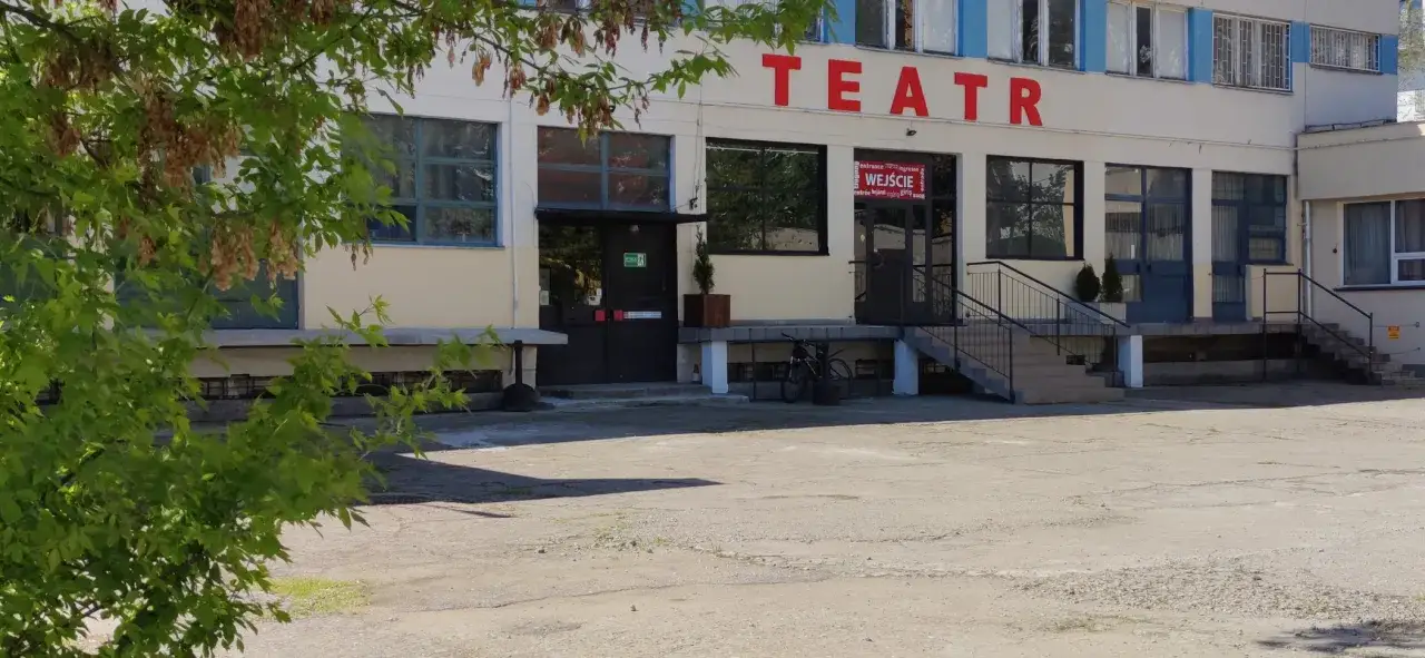 Teatr Druga Strefa, budynek z czerwonym napisem, wejście z wielojęzycznym szyldem, schody i rowery przed wejściem.