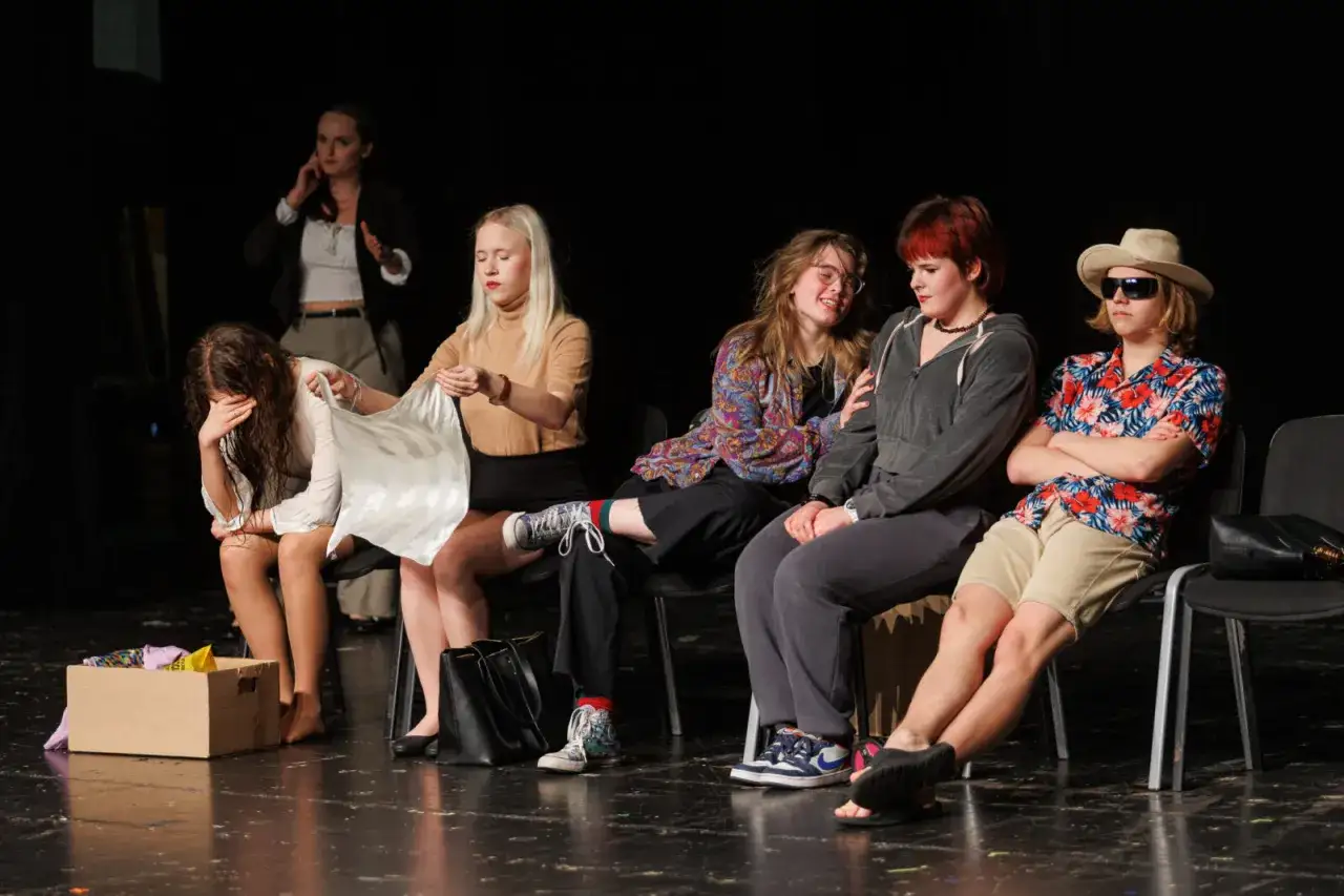Na scenie, w pudełku leżą ubrania. Dziewczyna w białej bluzce płacze, druga wyciąga białą tkaninę. Teatr nie ma scenariusza, ale emocje są prawdziwe.