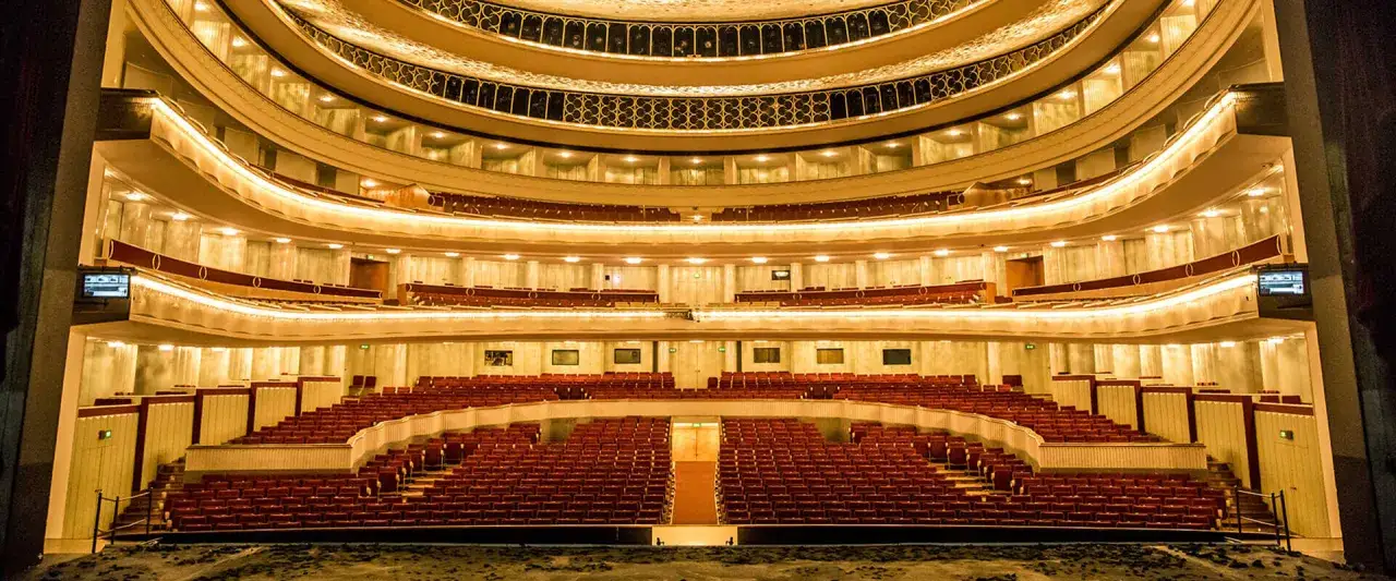 Wnętrze teatru z rzędami czerwonych foteli i złoconymi balkonami. Sprawdź opera warszawa repertuar, by zaplanować wieczór.