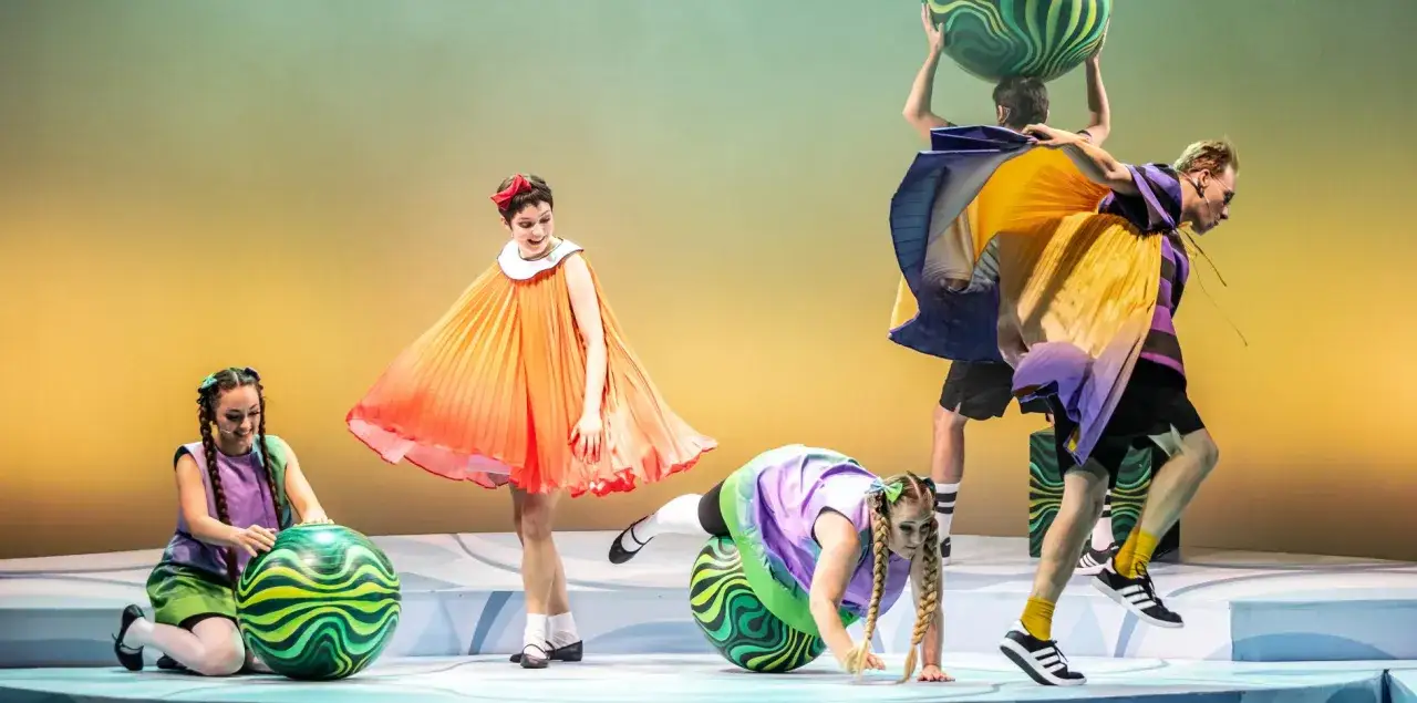 Opolski teatr lalki i aktora w barwnych strojach i z wielkimi piłkami na scenie.