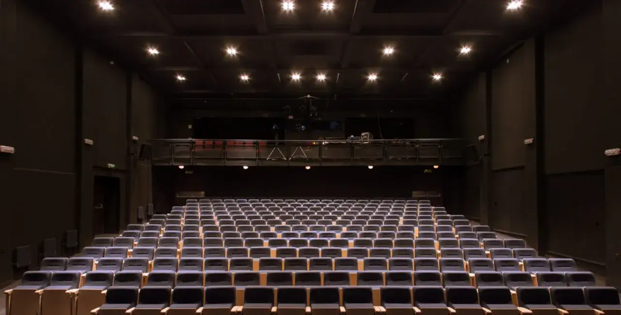 Puste rzędy siedzeń w Teatrze Miejskim im. Witolda Gombrowicza czekają na widzów. Wnętrze oświetlone jest punktowo z sufitu.