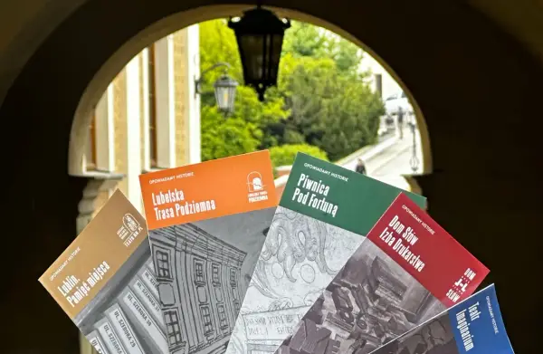 Książki o historii Lublina, m.in. "Lubelska Trasa Podziemna" i "Piwnica Pod Fortuną", prezentowane na tle bramy. Teatr NN Lublin zaprasza do odkrywania przeszłości.
