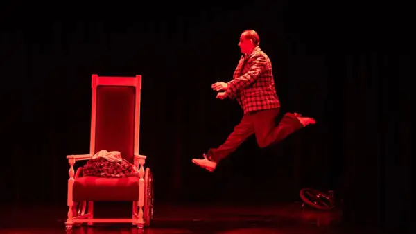 Aktor w skoku na scenie Teatru Komedia Kraków. Czerwone światło podkreśla dynamikę sceny.